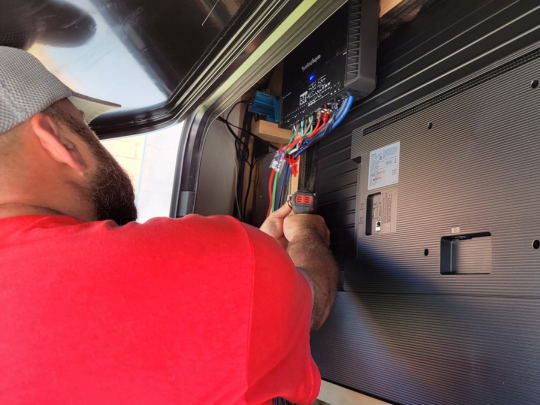 Installing a Rockford Fosgate amplifier behind the TV installation.